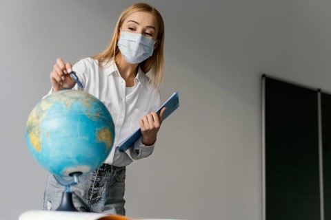 Female teacher classroom with clipboard pointing globe