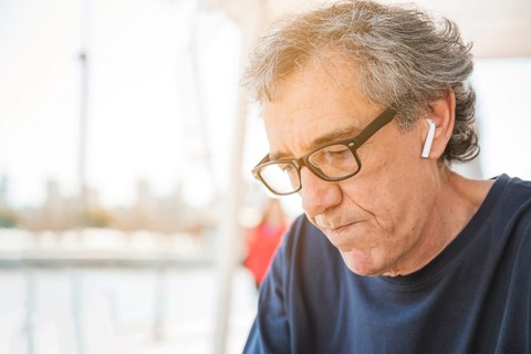 Senior man wearing eyeglasses with white bluetooth earphone his ear