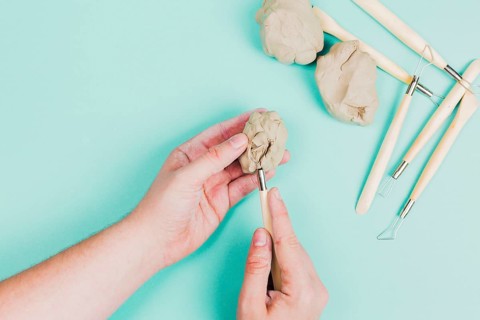Close up person s hand using sculpting tools mint green background