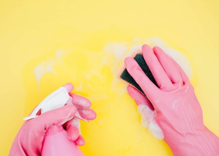 Close up cleaner cleaning yellow backdrop with sponge spray bottle