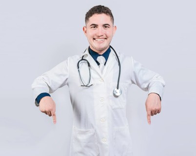 Young doctor pointing a promotion down. Happy doctor pointing fingers down. Latin doctor pointing down an isolated advertising space