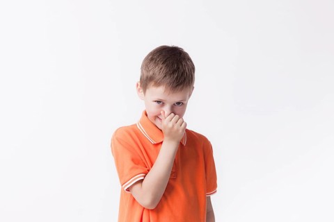 Boy closing his nose with fingers looking camera white background