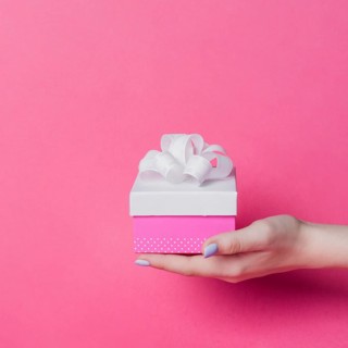 Female s hand holding box with white ribbon bow pink background