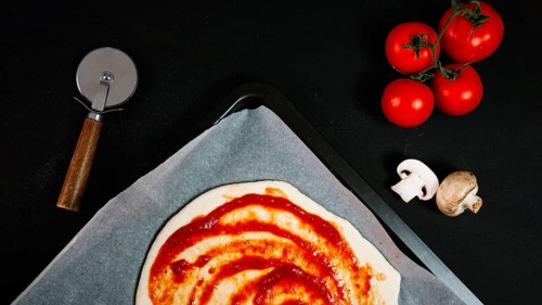 Pizza dough with sauce near vegetables