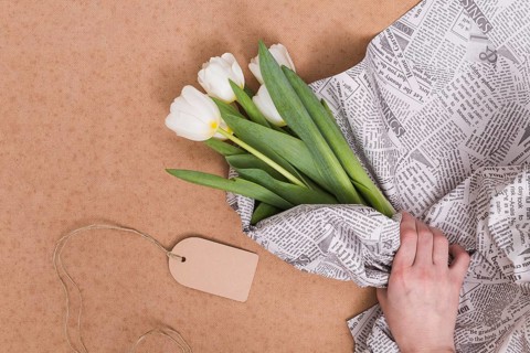 Person s hand wrapping white tulip flowers newspaper with price tag brown background