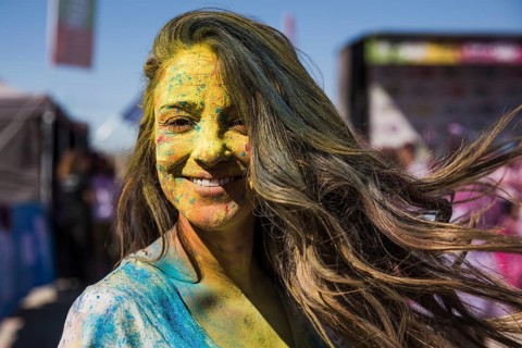 Smiling young woman covered her face with holi color looking camera