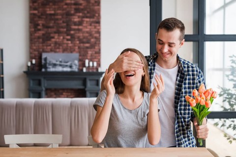 Man with flowers surprising cheerful woman