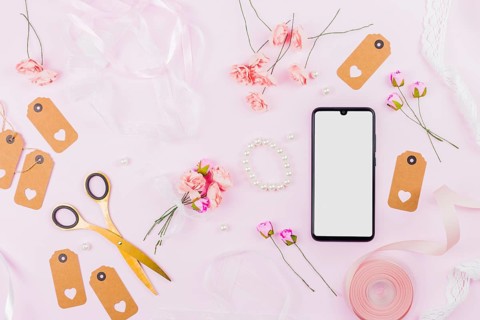 White screen display mobile phone with ribbons roses tags pearl pink backdrop