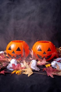 Halloween pumpkins over red autumn leaves and ghosts with smoke on a black background
