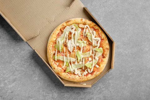 Top view of vegetarian pizza with iceberg lettuce and tomato slices in cardboard box