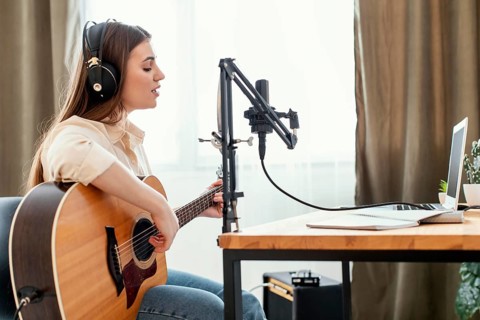 Female musician recording song home while playing acoustic guitar