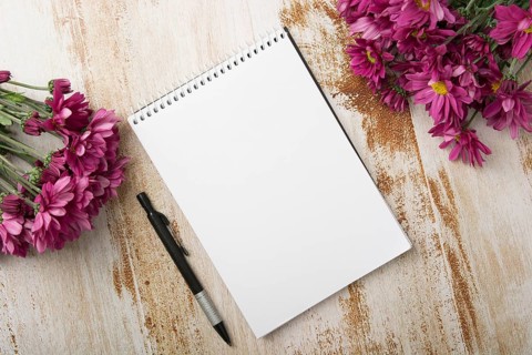 Overhead view spiral notepad with pen pink flowers wooden background
