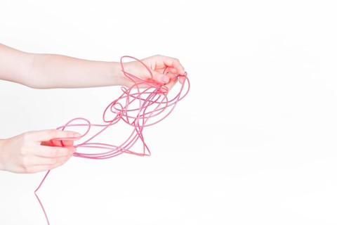 Human hand trying untangle red wire white background