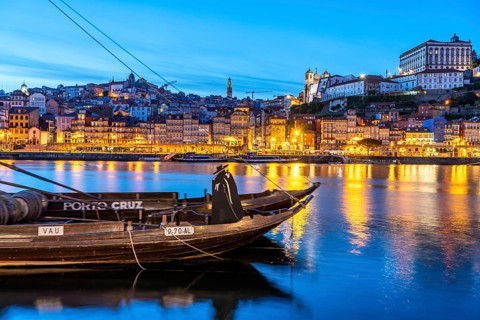 View over the traditional Rabelo boats on the Douro riverbank in Vila Nova de Gaia towards the old town of Porto at dusk