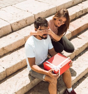Woman covering her boyfriend s eyes surprising him with gift