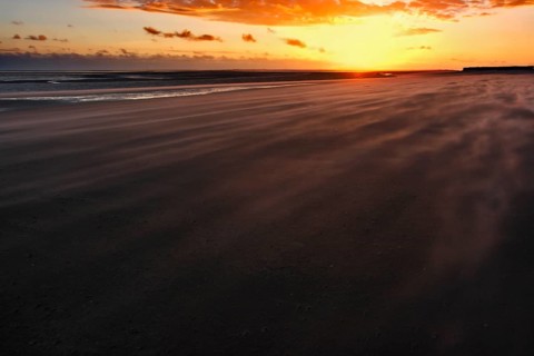Sand drifting on the beach of the island of Minsener Oog at sunset