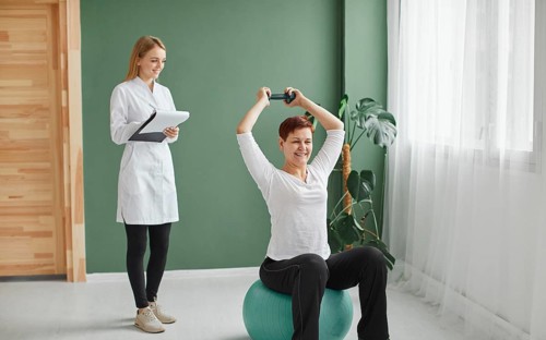 Elder woman covid recovery doing physical exercises with dumbbell while nurse checks