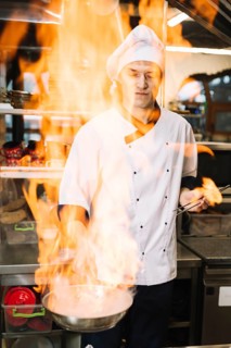 Young cook holding burning pan hand