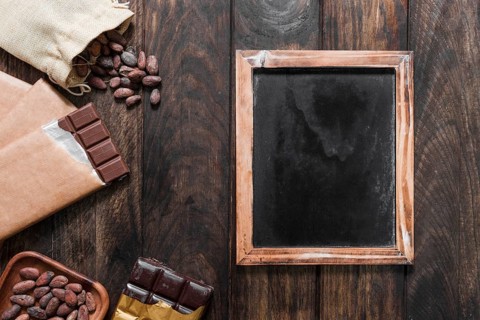 Blank wooden slate with cocoa beans chocolate bars wooden table