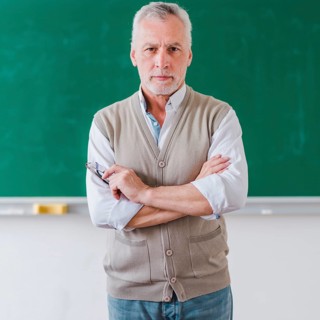 Senior male professor with arms crossed standing against chalkboard