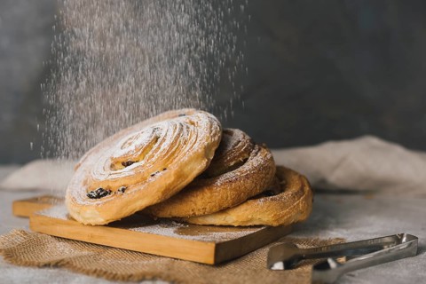 Close up sugar dusting baked cinnamon buns chopping board
