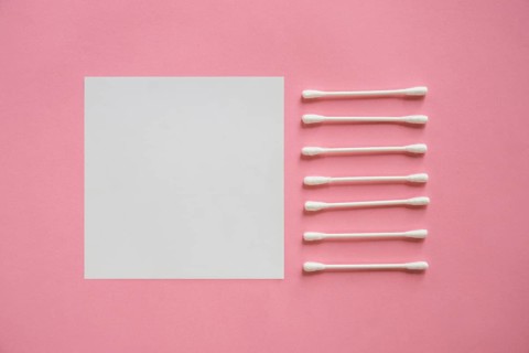 Row cotton swabs near blank adhesive note pink background