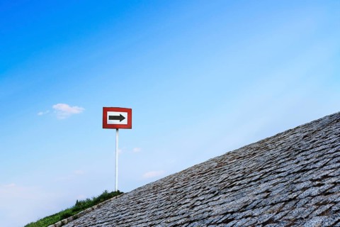 Black arrow on white background and in red frame standing atop of cobblestone paved hill at day. Blue sky with great clouds. Copy space