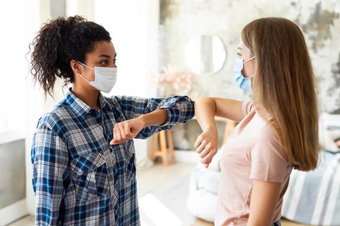Side view female friends with medical masks practicing elbow salute