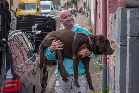 Young man carries his sick dog to the car