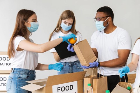 Volunteers with gloves medical masks preparing box with food donation
