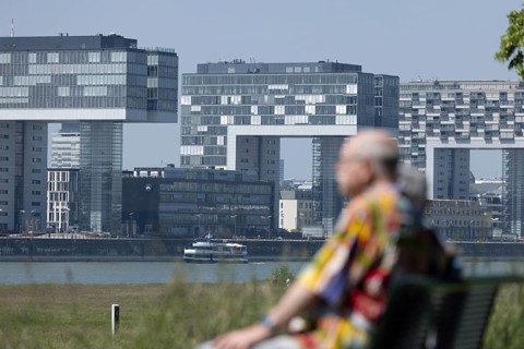 Senior couple sitting on a bench on the banks of the Rhine in front of the crane houses in Cologne's Rheinauhafen harbour on the other bank
