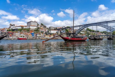 View over the traditional Rabelo boats on the Douro riverbank in Vila Nova de Gaia towards the old town of Porto and the bridge Ponte Dom Luis I