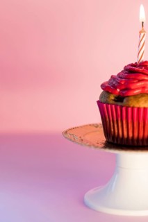 Close up lighted candle cupcake cakestand against pink background