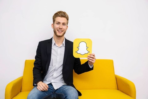 Portrait young man sitting yellow sofa holding snapchat icon