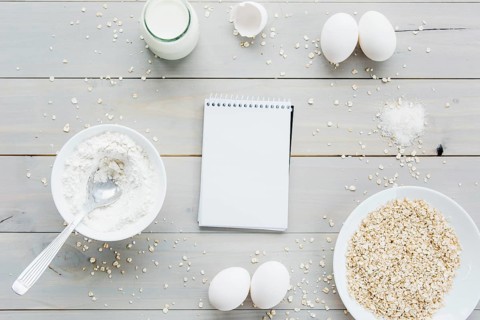 High angle view spiral notepad oats eggs flour milk wooden backdrop