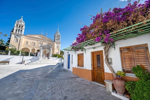 White Cycladic house with purple bougainvillea and Agia Triada church
