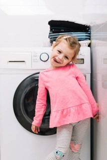 Portrait cute girl standing front washing machine