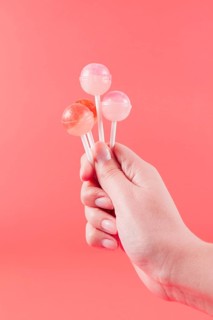 Close up woman s hand holding lollipops against coral backdrop