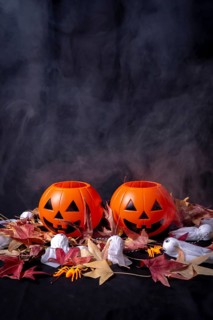 Halloween pumpkins over red autumn leaves and ghosts with smoke on a black background