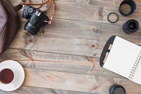 Top view dslr camera cup tea spiral notepad pen camera lens bag wooden table