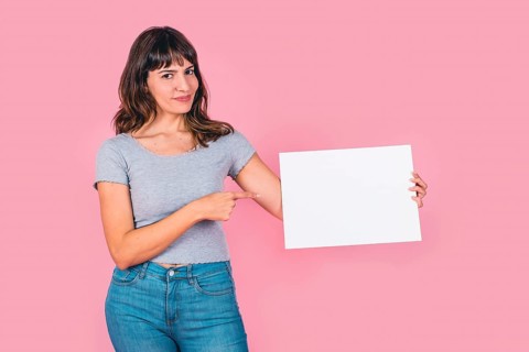 Beautiful woman pointing at a blank whiteboard against a pink background