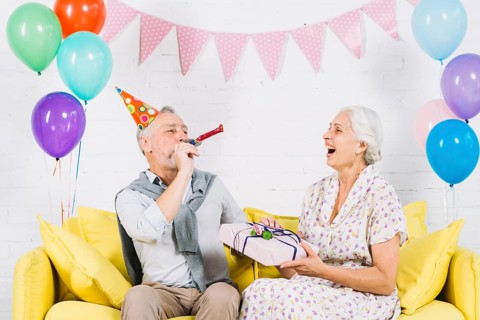 Happy woman with birthday gift looking her husband blowing party horn