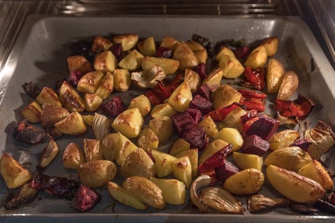 Vegetables and jacket potatoes on a baking tray in the oven