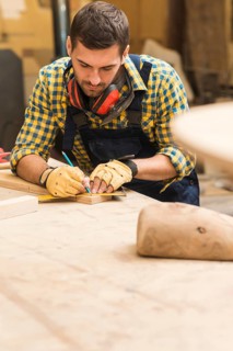 Male carpenter measuring wooden block with ruler pencil