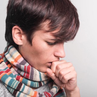 Woman wearing multicolored scarf around neck coughing against gray backdrop