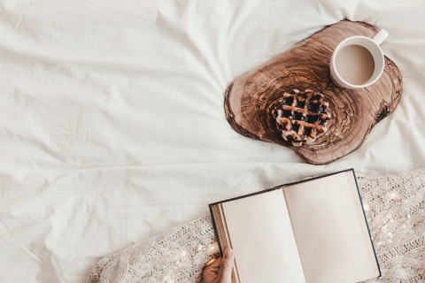 Hand with notebook near biscuit hot drink stand bedsheet