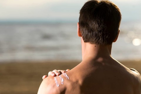Back view man applying sunscreen lotion