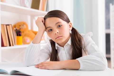 Tired schoolgirl doing homework desk