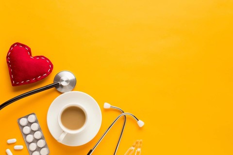 Coffee cup blister packed tablets stethoscope stitched heart shape against yellow background