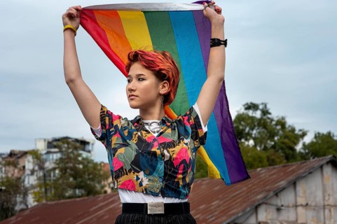Front view redhead non binary person holding lgbt flag